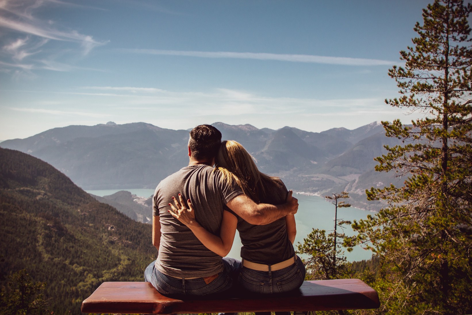 Dos personas abrazadas, contemplando un paisaje de montañas y un lago.